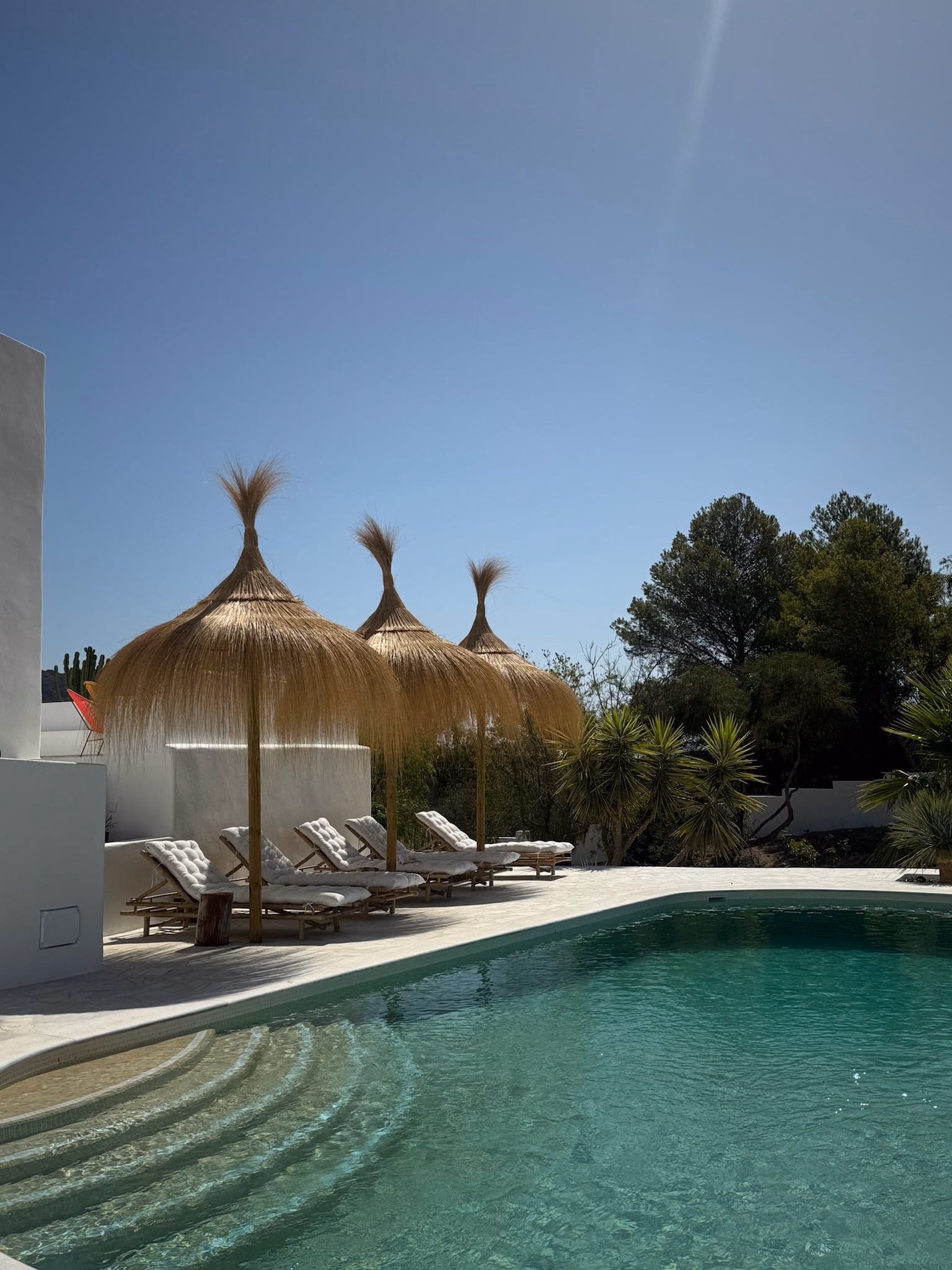 Transats sous des parasols en paille au bord des marches de la piscine