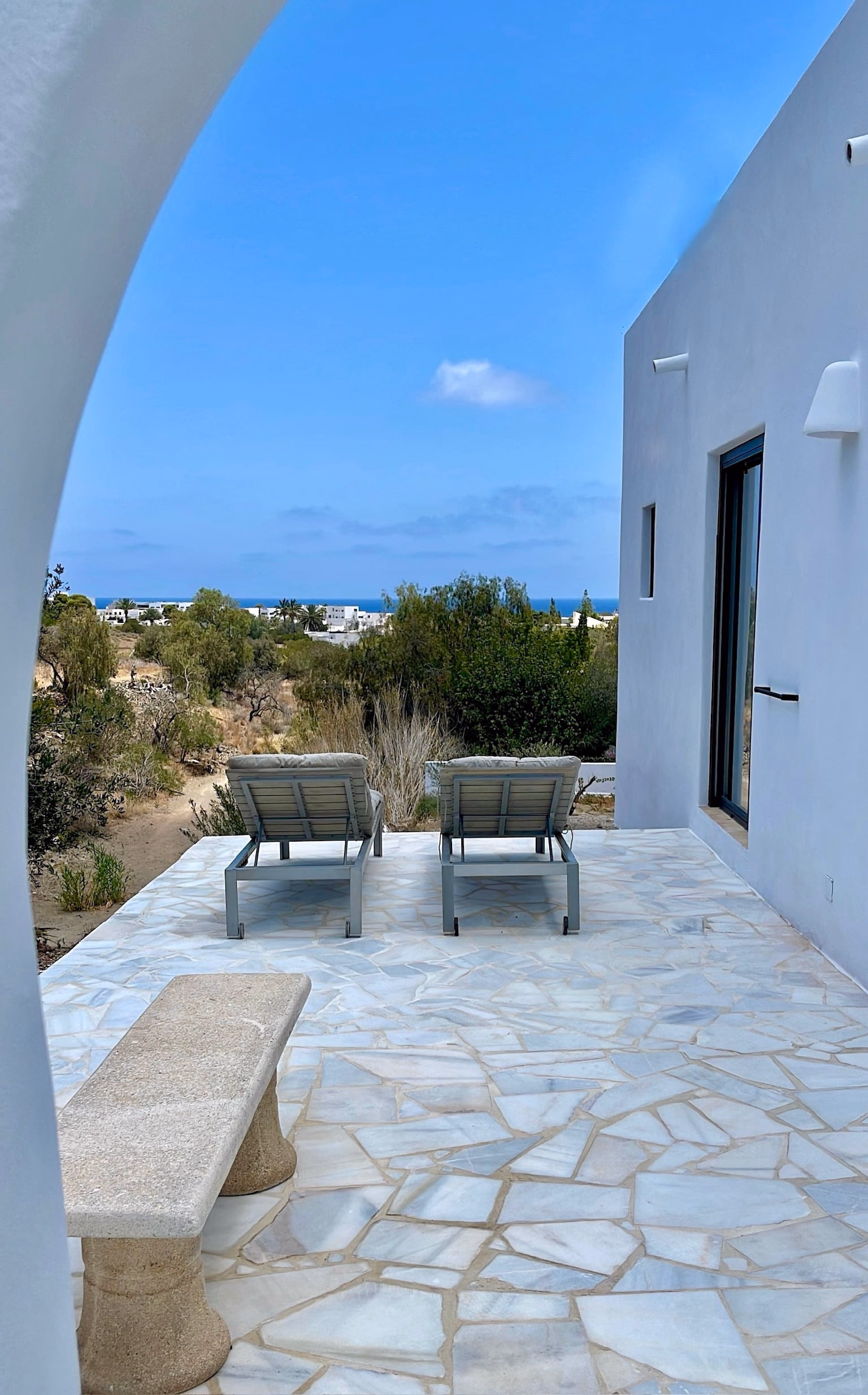Terrasse dallée avec deux transats et un banc en pierre, la mer à l’horizon