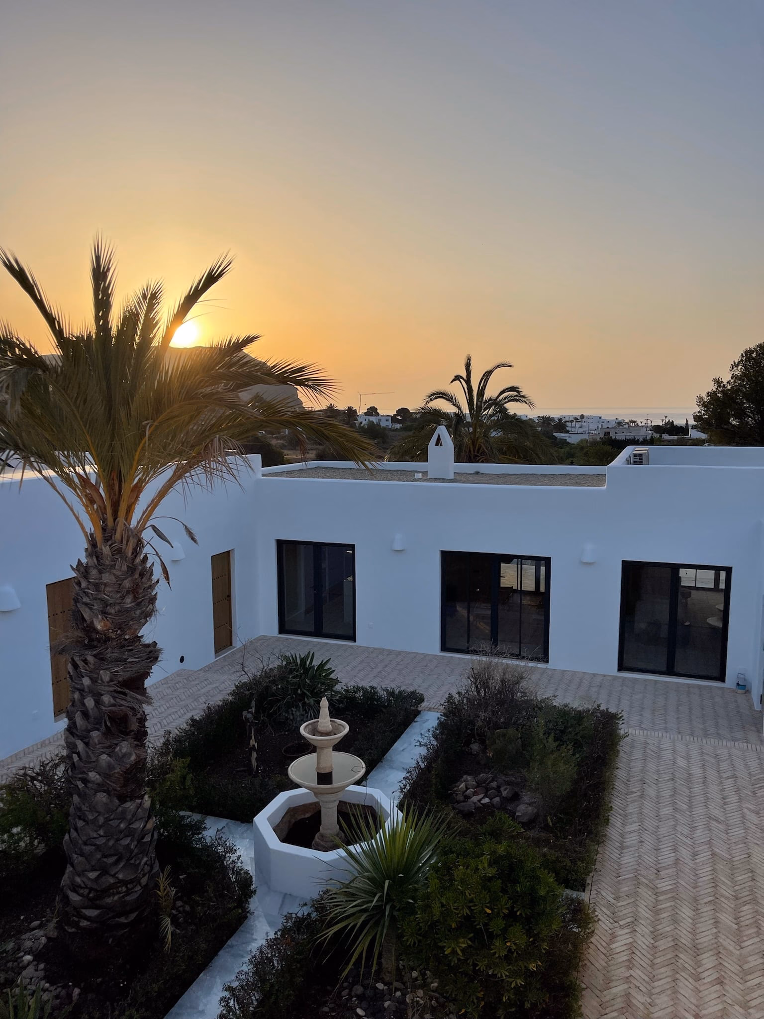 Palmier au coucher du soleil au-dessus du patio et de sa fontaine