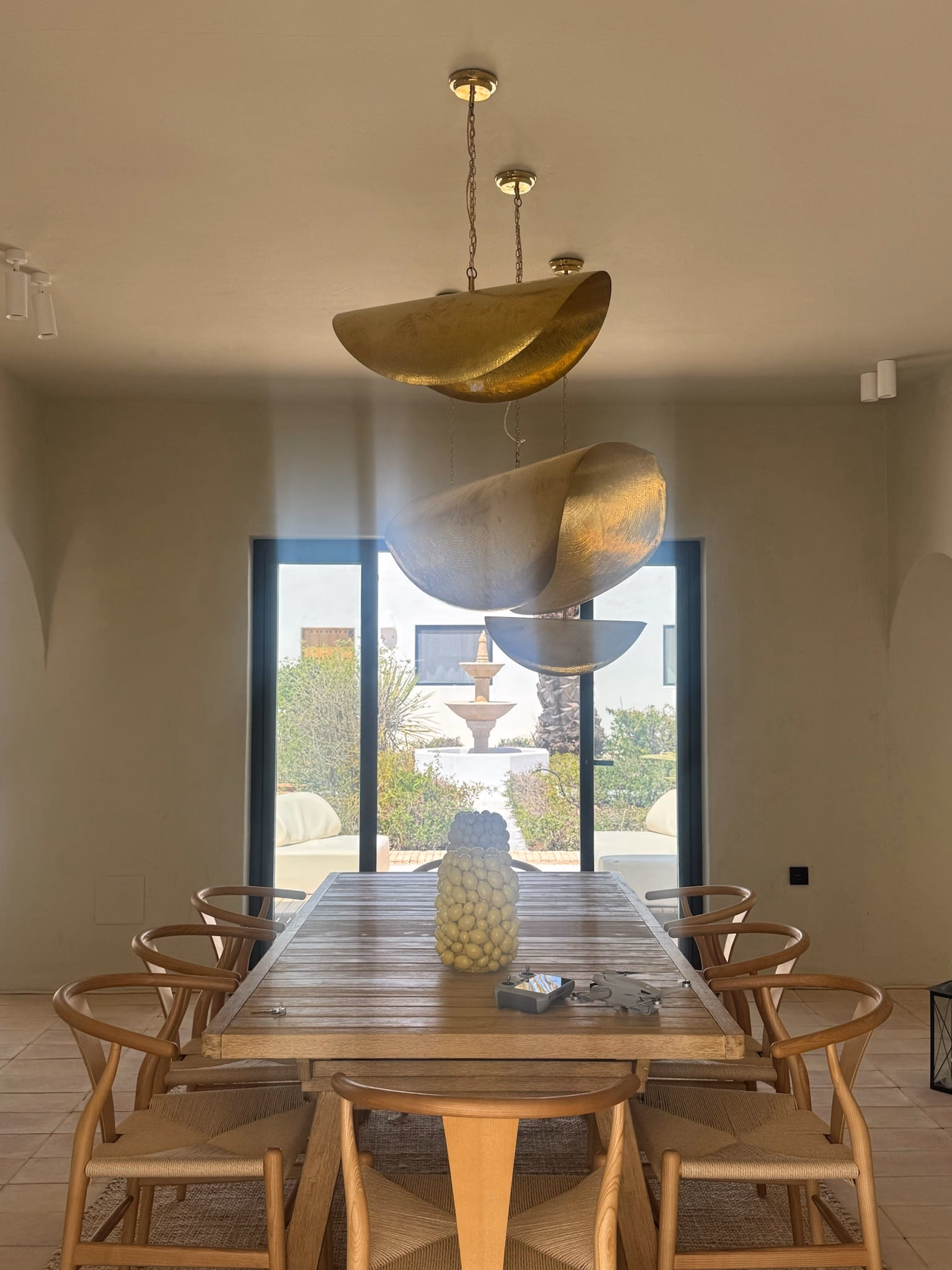 Salle à manger avec longue table en bois, chaises en bois et suspensions en laiton