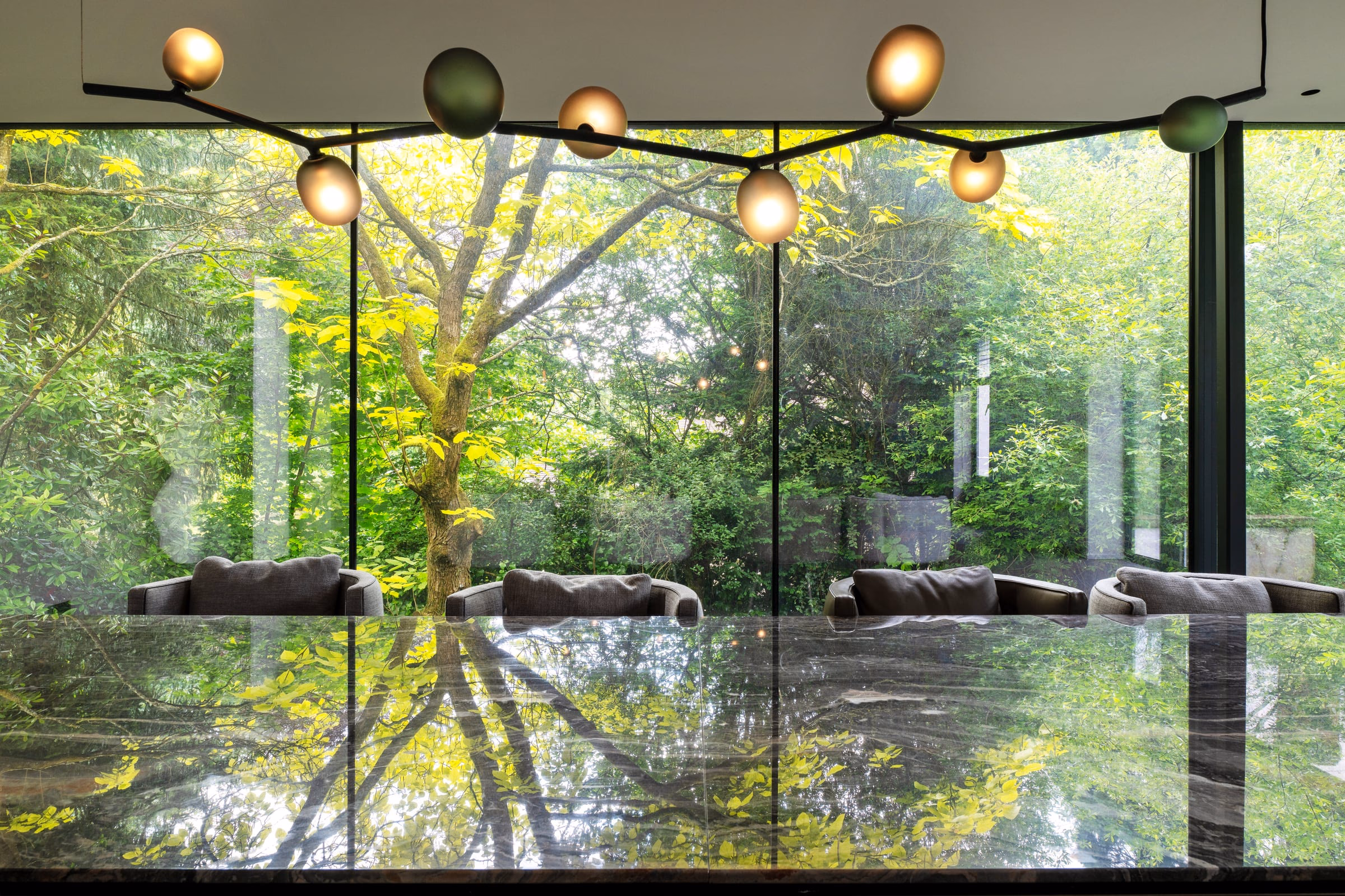 A glass-walled dining room under a ring of globe pendants, trees beyond
