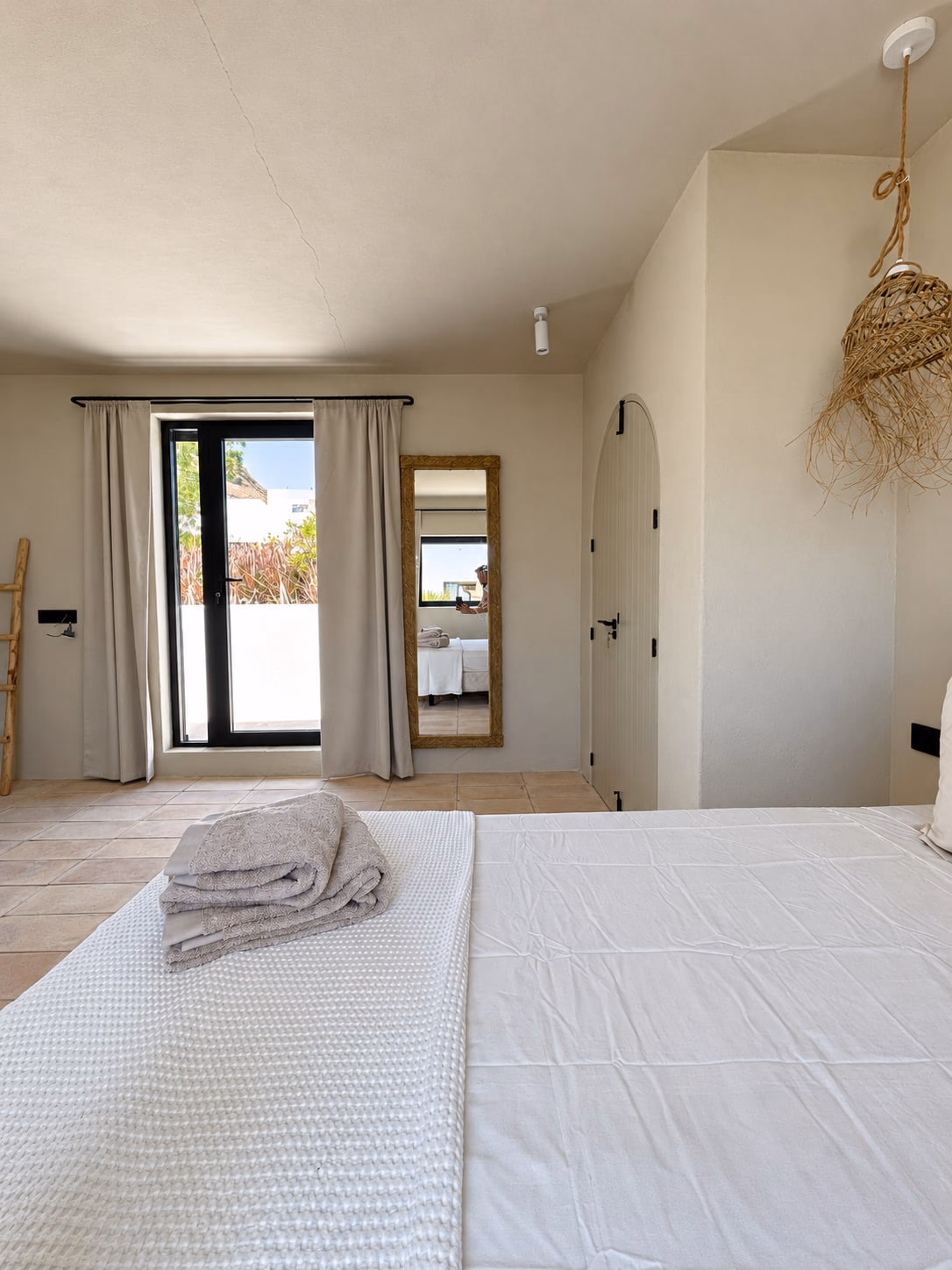 Chambre avec lit blanc et linge plié, une haute fenêtre au fond