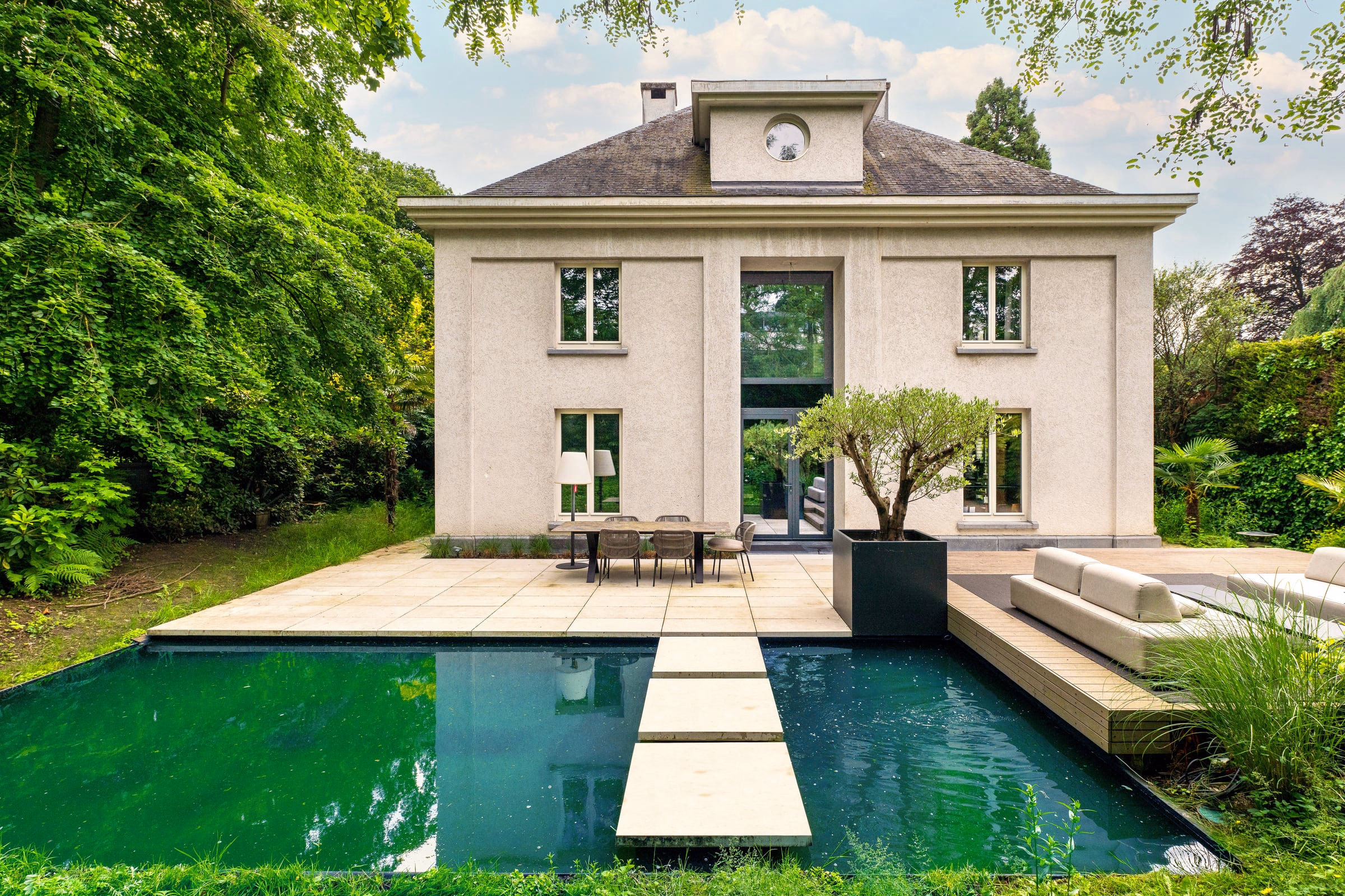 A white house reflected in a dark mirror pool, stepping stones crossing the water