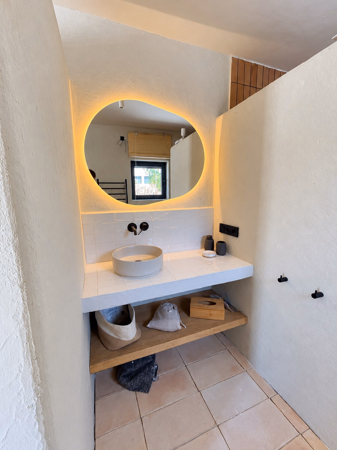 Miroir de forme organique éclairé au-dessus d’un meuble-lavabo enduit