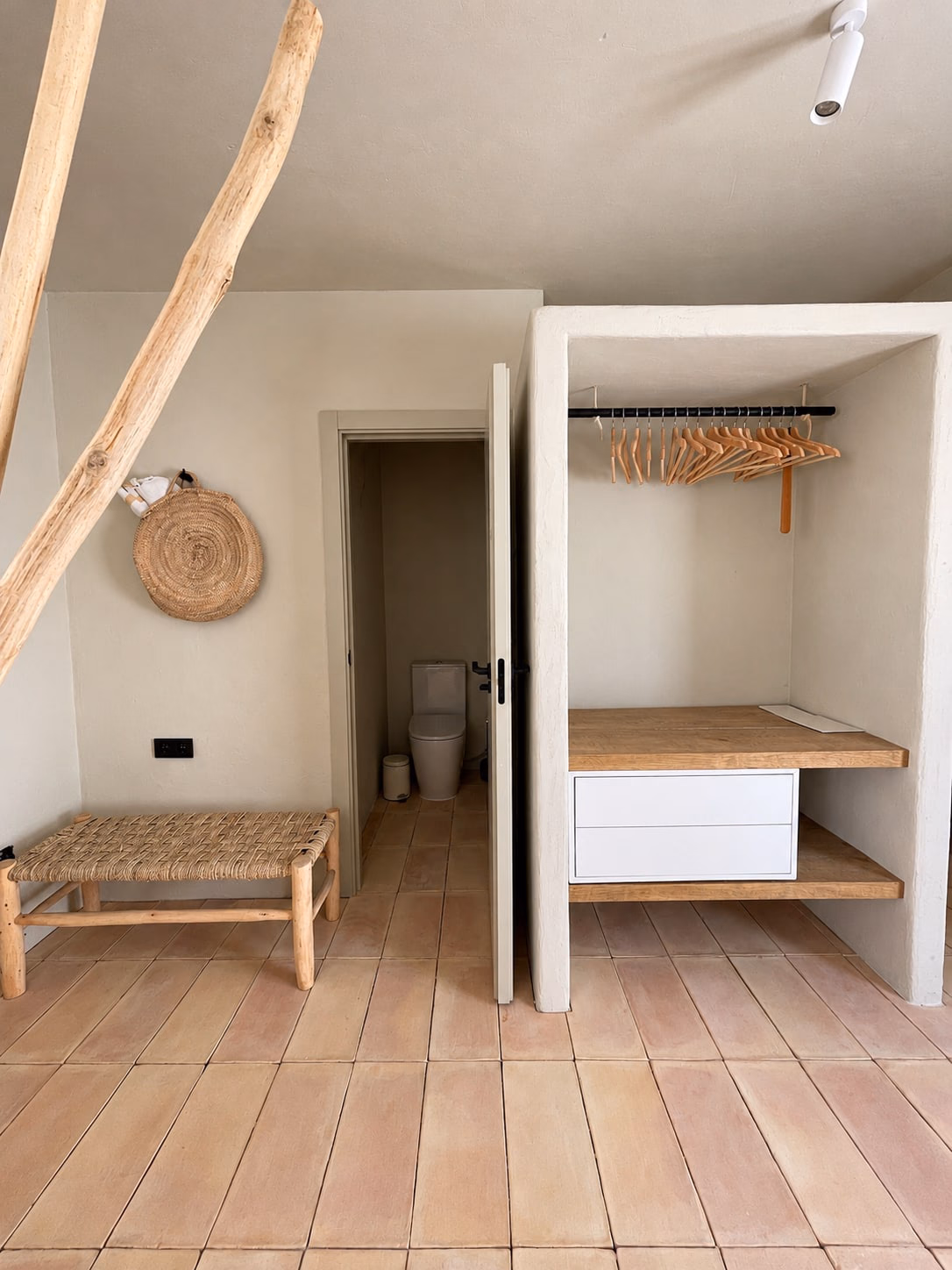 Niche de rangement avec banc tressé, les toilettes visibles par la porte