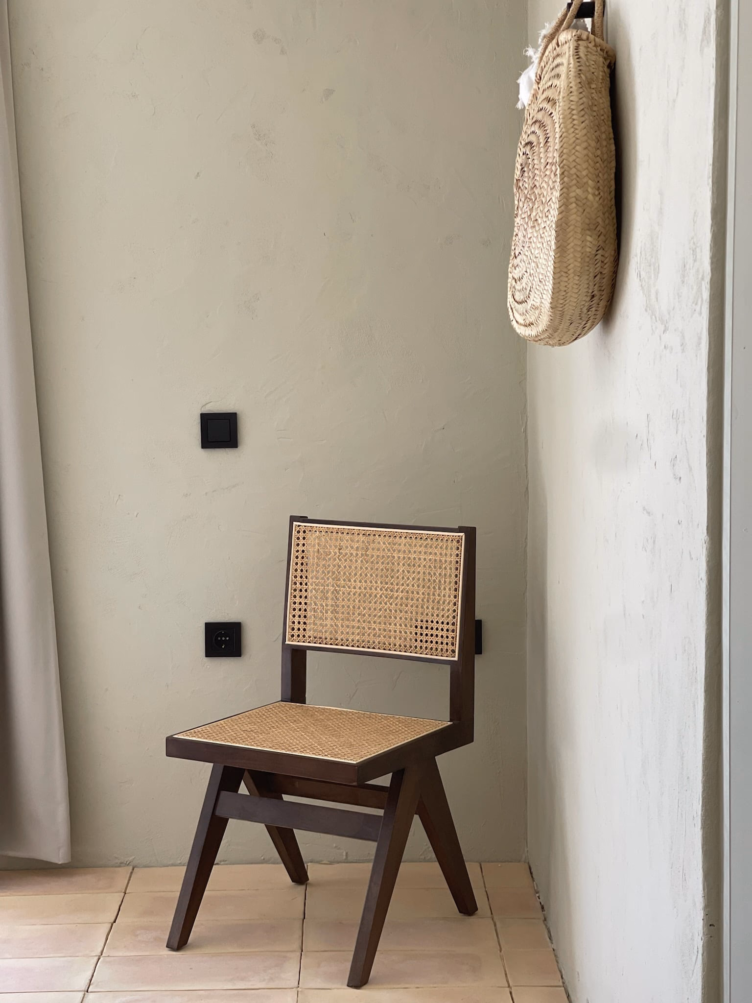 Chaise cannée contre un mur enduit, un panier tressé accroché à côté